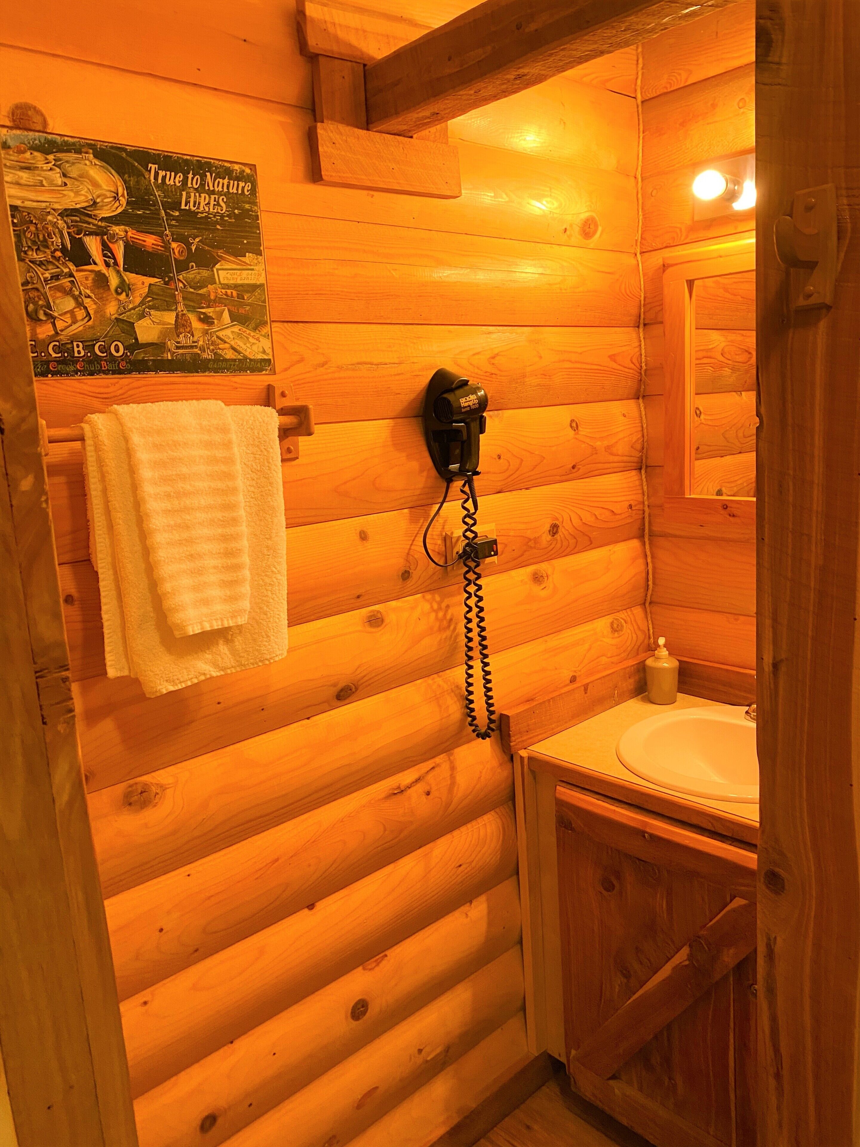 Une salle de bain rustique, avec des murs en bois, un lavabo blanc, une serviette suspendue à un porte-serviettes et une affiche ancienne.