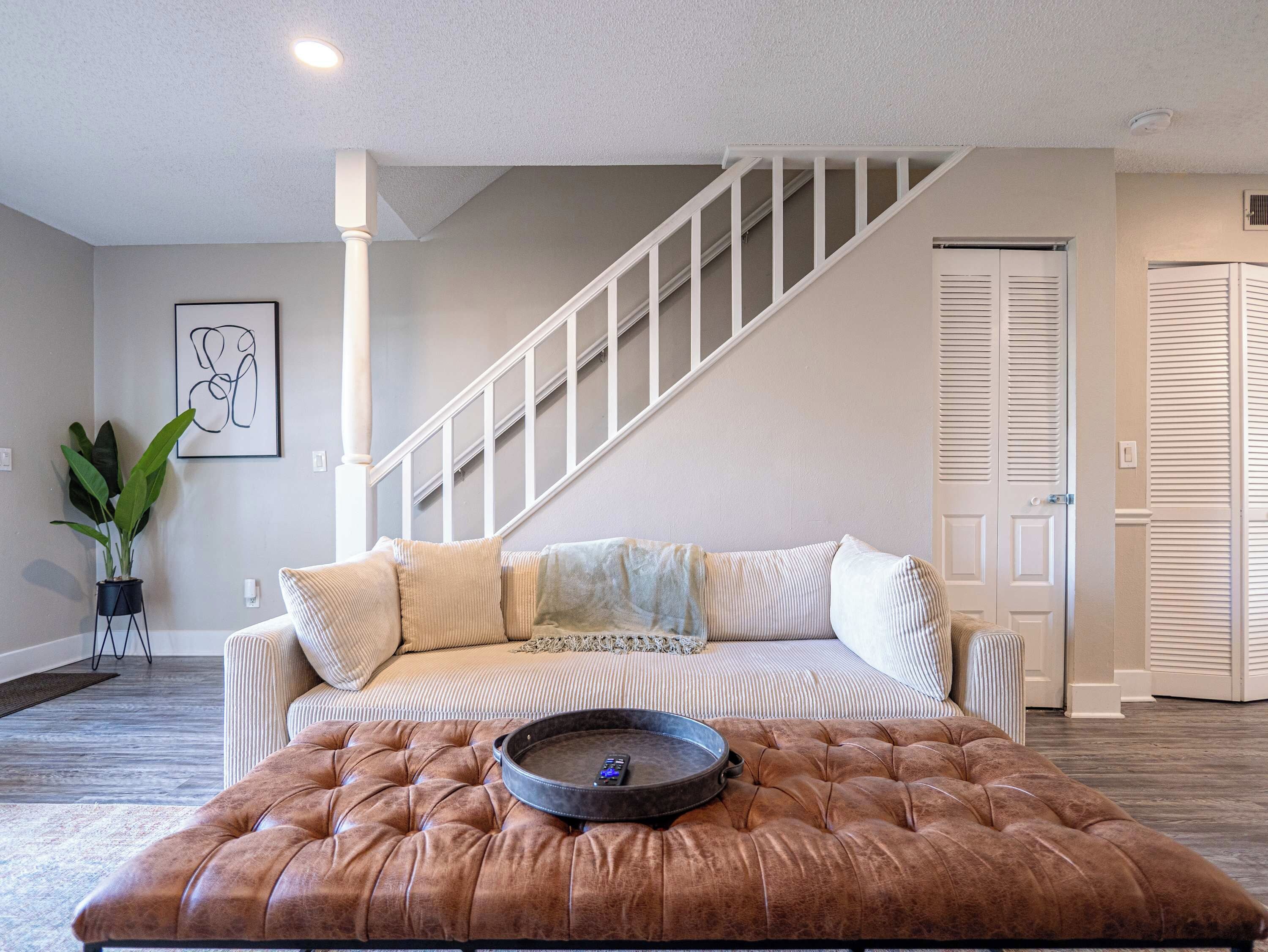 Un salon avec un canapé, un pouf et un escalier.