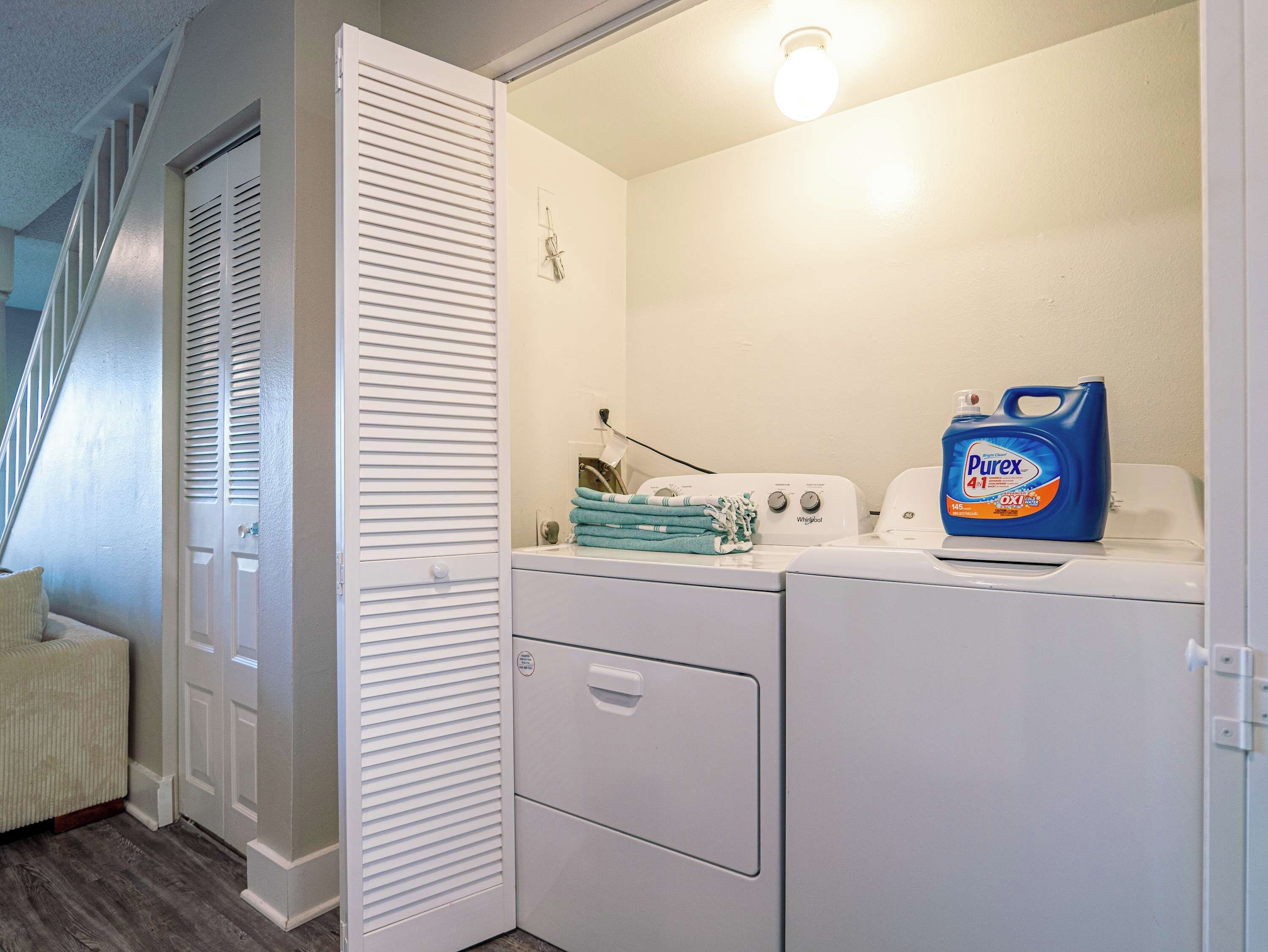 A laundry room with a washing machine, dryer, and a bottle of Purex detergent.