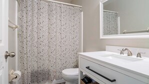 Un baño con lavamanos blanco, espejo, inodoro y cortina de ducha con diseño moteado.