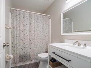 Un baño con lavamanos blanco, espejo, inodoro y cortina de ducha con diseño moteado.