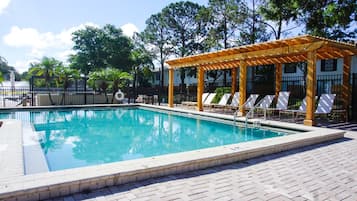 A swimming pool with a wooden pergola and lounge chairs.