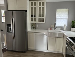 A modern kitchen with a stainless steel refrigerator, white cabinetry, a built-in dishwasher, and a window with blinds.