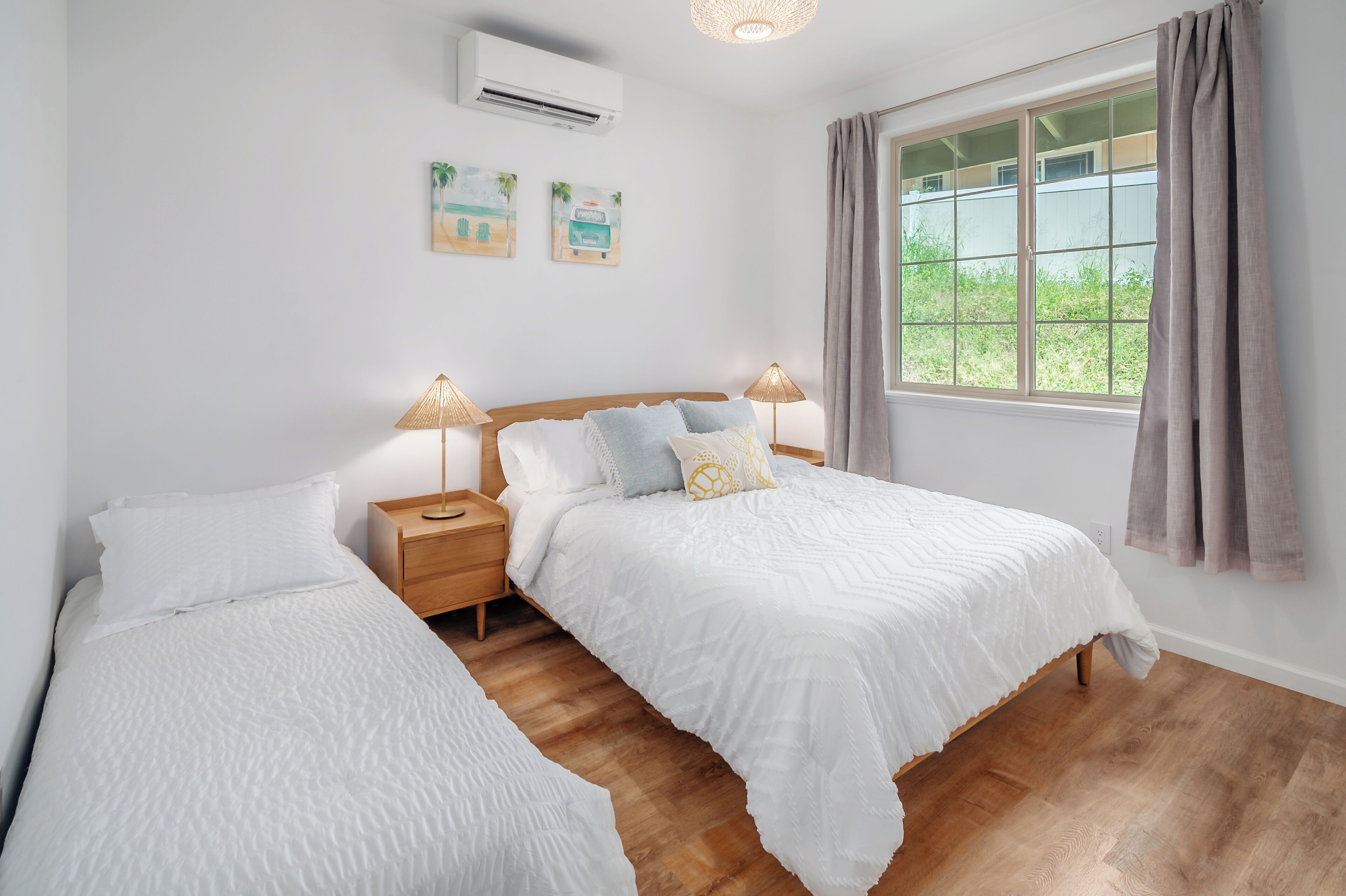 A bedroom with two beds, wooden flooring, a window with curtains, and wall-mounted air conditioning.