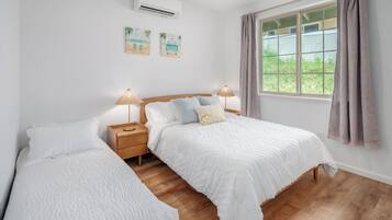 A bedroom with two beds, wooden flooring, a window with curtains, and wall-mounted air conditioning.