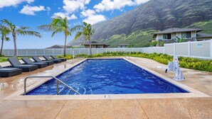 Una piscina con sillas de descanso, palmeras y montañas al fondo.