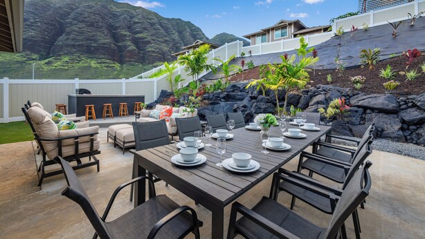 Un área de comedor al aire libre con vistas a un paisaje montañoso, una valla blanca y una casa con balcón.