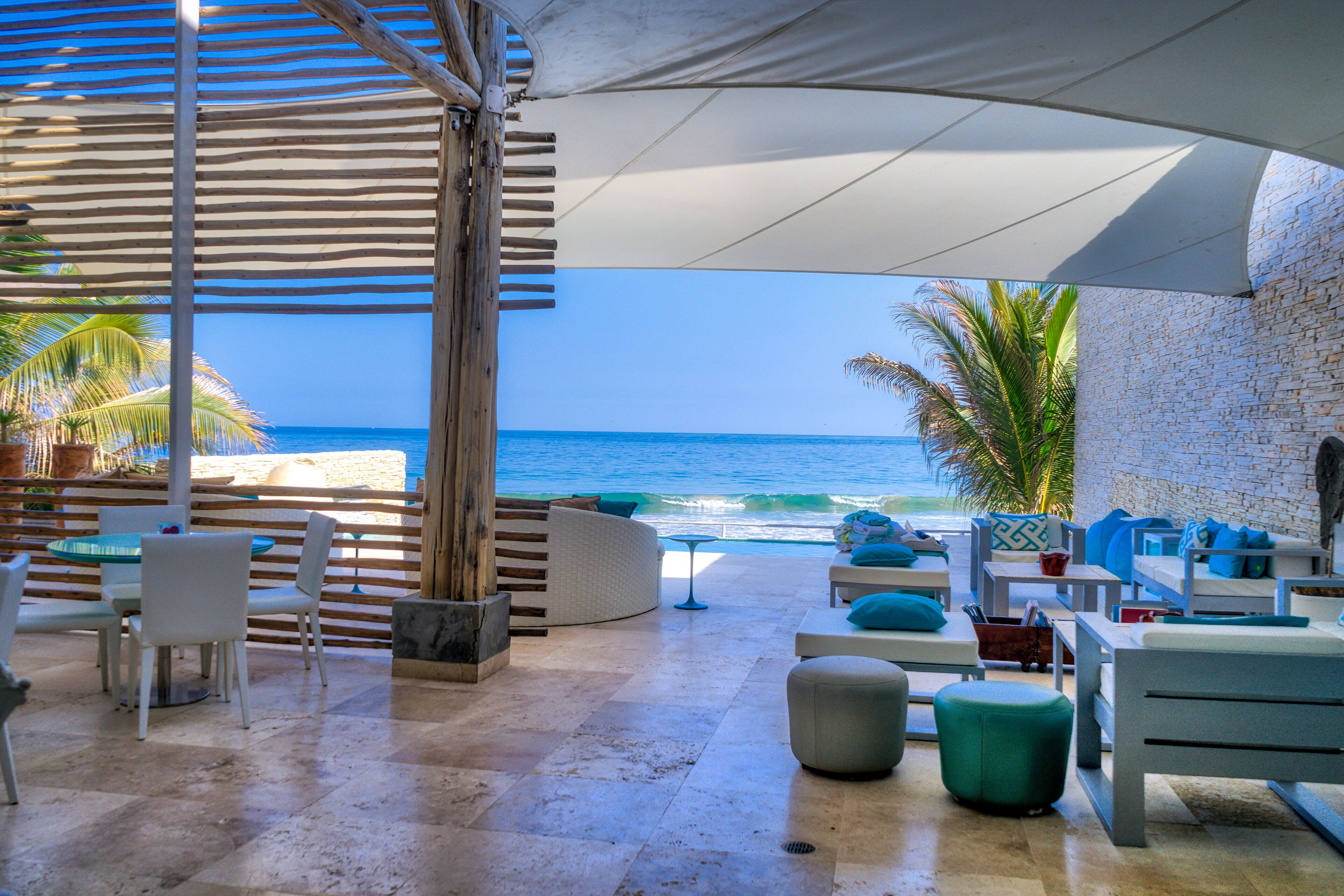 Een strandlounge met uitzicht op de oceaan, met een zithoek met tafels en stoelen, een klein tafeltje en een comfortabele bank.