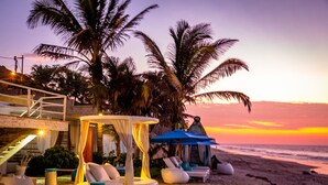 Un salon de plage doté d’un espace salon circulaire, d’un auvent et offrant une vue sur l’océan au coucher du soleil.