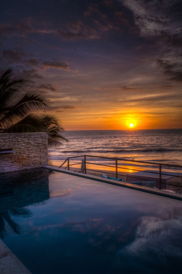 A sunset over the ocean with a pool and palm trees. - DCO Suites Lounge & Spa (Máncora)