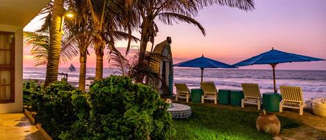 A beachside patio with palm trees, a gazebo, and lounge chairs under umbrellas.