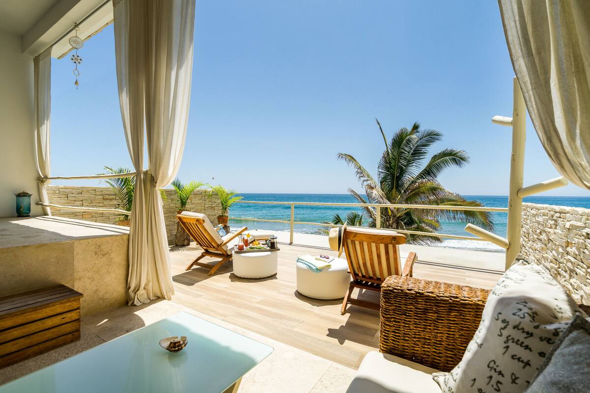 A balcony with wicker furniture, a small table, and a view of the ocean.