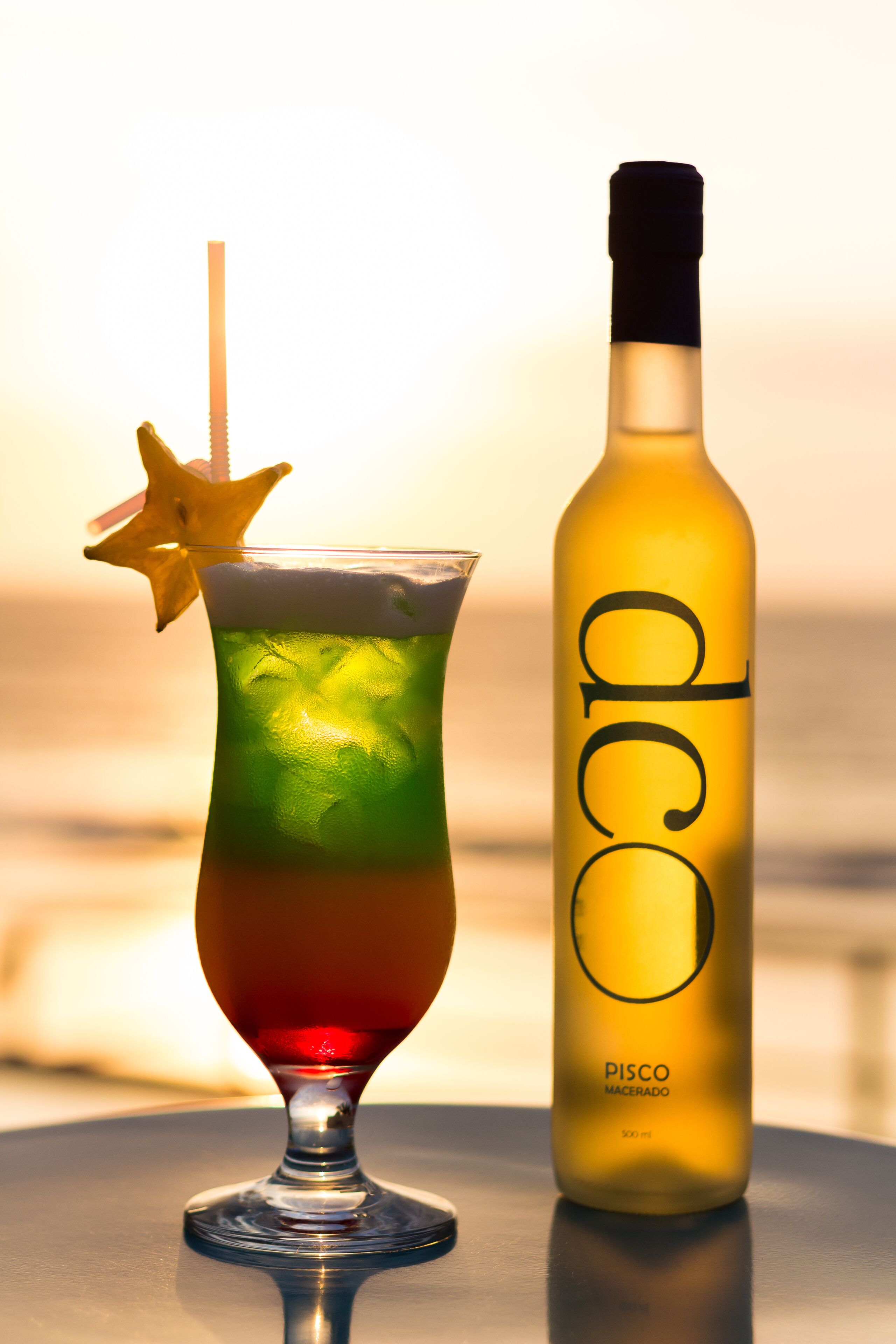 A cocktail glass with a star garnish and a bottle labeled "Pisco Macerado" beside it.