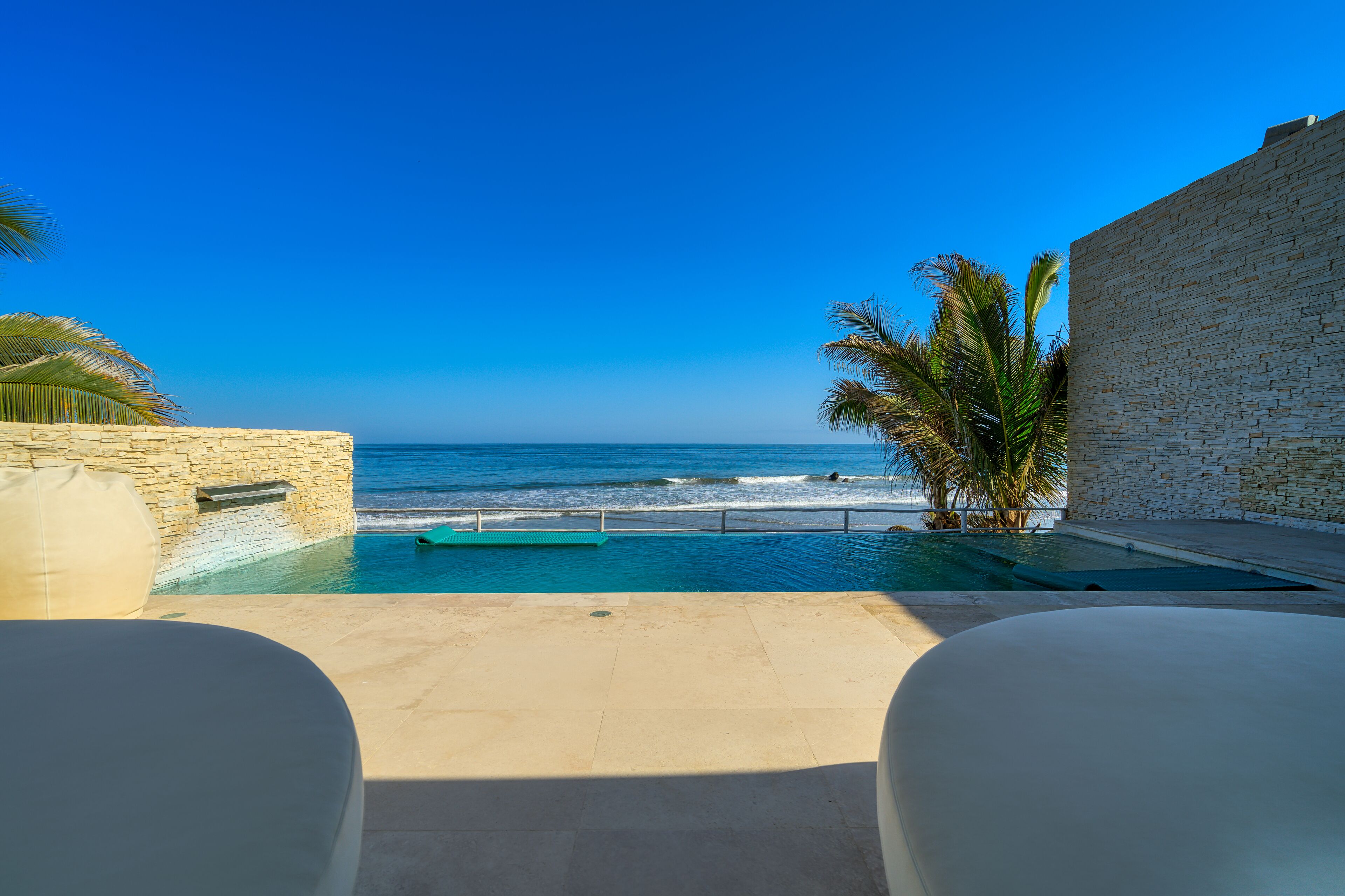 Ein Pool mit Blick auf den Ozean, eine Steinmauer und eine Palme.