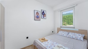Un dormitorio con cama, una ventana con vista a vegetación y dos cuadros en la pared.