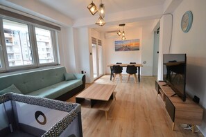 Una sala de estar moderna con un sofá, una mesa de comedor con sillas, un televisor y un cuadro en la pared.