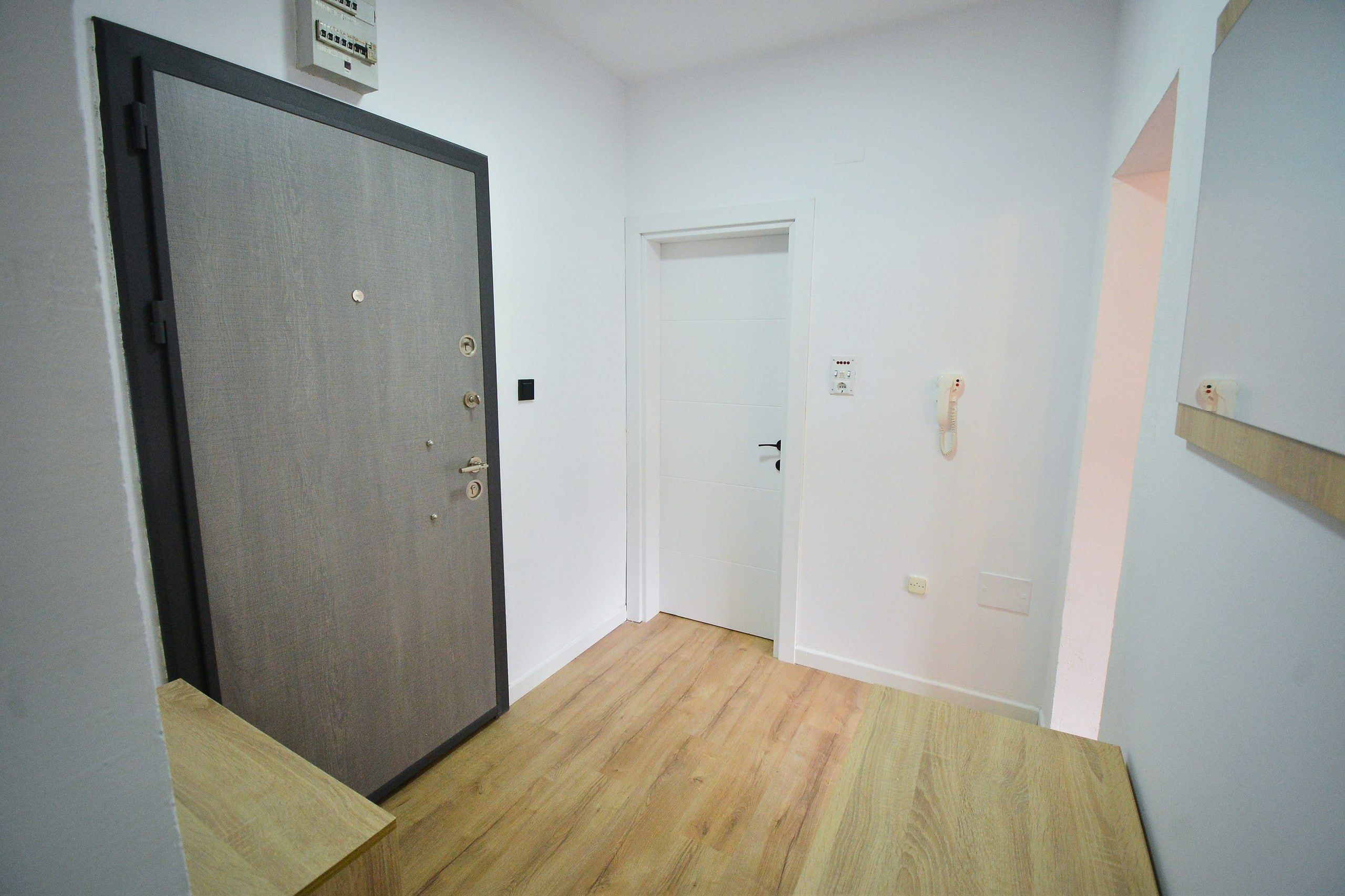 Un pasillo con piso de madera, una puerta cerrada con un letrero encima y una pared blanca con un interruptor de luz y un teléfono.