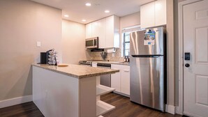 A modern kitchen with white cabinets, a stainless steel refrigerator, a microwave, and a granite countertop. - Townhouse | USF - Moffitt - AdventHealth - Busch Gardens (Tampa)
