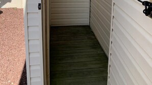 Un espace extérieur étroit et clos, doté d’un plancher en bois, d’une échelle en métal et d’un robinet fixé au mur.