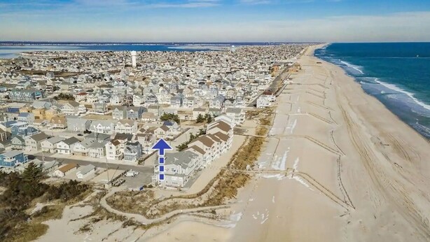Vue aérienne d’une zone résidentielle côtière, avec des maisons, une plage et un phare.