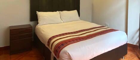 Una cama con cabecera oscura, dos mesitas de noche y una colcha estampada.