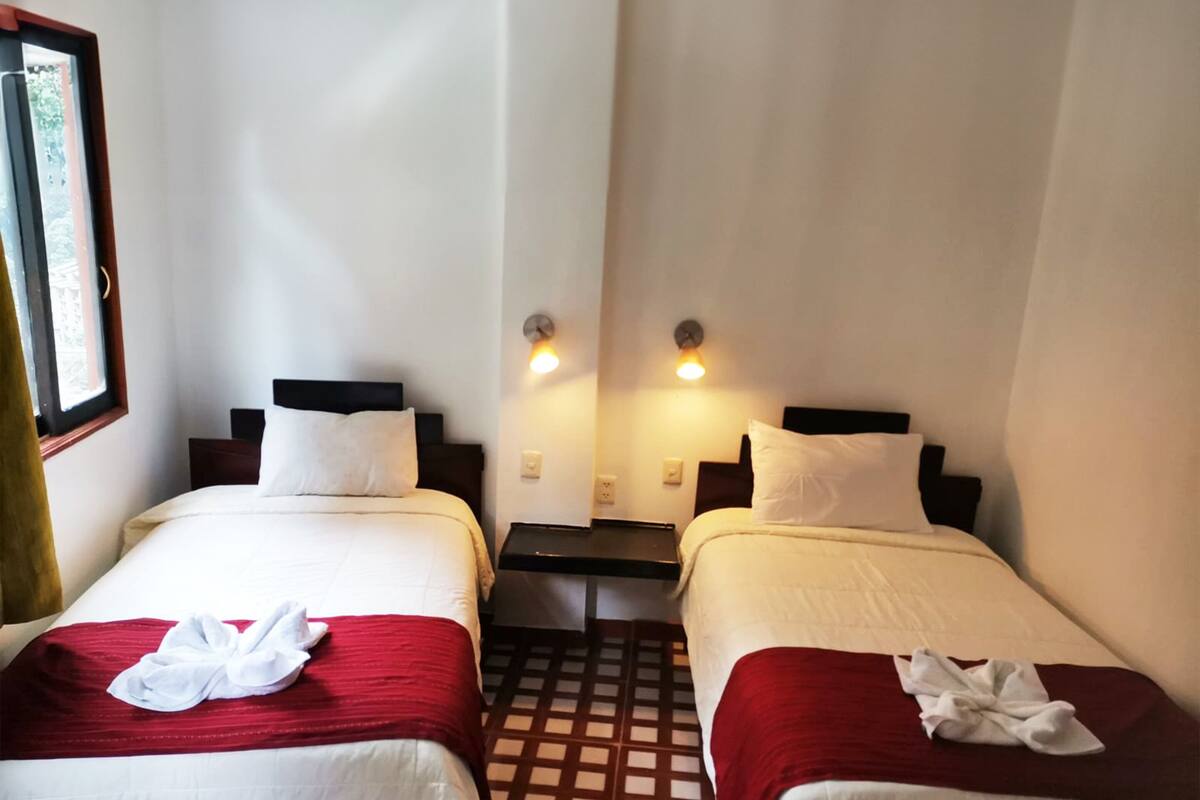 A hotel room with two beds, each with a red and white bedspread, and a window on the left side.
