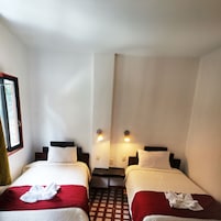 Une chambre d’hôtel avec deux lits, chacun recouvert d’une couverture rouge et blanche, et une fenêtre située sur le côté gauche.