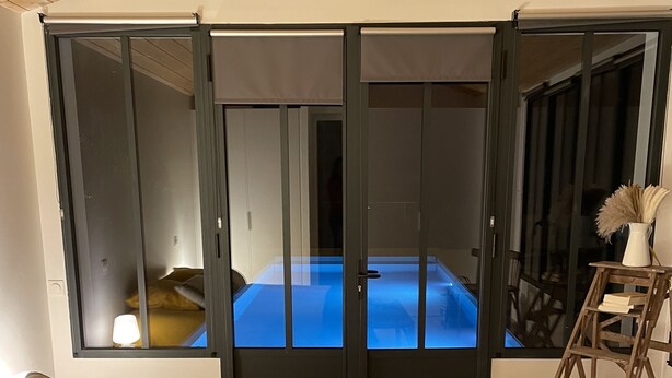 Ein Schlafzimmer mit einem Bett, einer Bank, einer Leiter und Blick auf einen blau beleuchteten Raum durch eine Schiebetür.