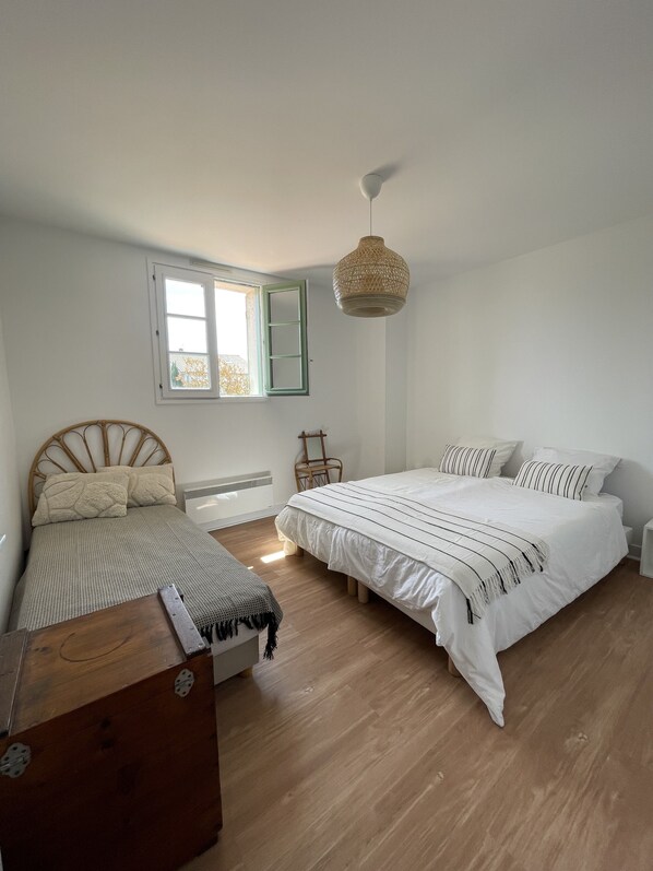 Une chambre à coucher avec un grand lit, un plus petit lit, une commode en bois, une chaise et un luminaire suspendu.
