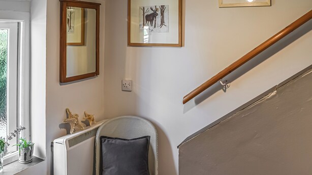 A stairwell with a wooden handrail, a radiator, a chair with a cushion, and a framed picture on the wall.