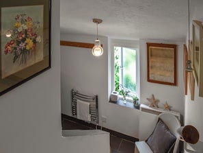 Una habitación con una cama, una silla, un ventanal con plantas, una lámpara en el techo e imagen enmarcada en la pared.