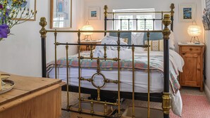 A bedroom with a four-poster bed, a wooden nightstand, a bedside table, and a wall-mounted lamp.