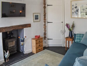 A living room with a fireplace, a television, a wooden cabinet, a sofa, and a small table with a vase. - 1 bedroom accommodation in Benllech (Benllech)