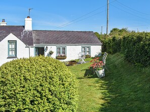 A white house with a grey roof, a chimney, and a small garden with a hedge and a flower pot. - 1 bedroom accommodation in Benllech (Benllech)