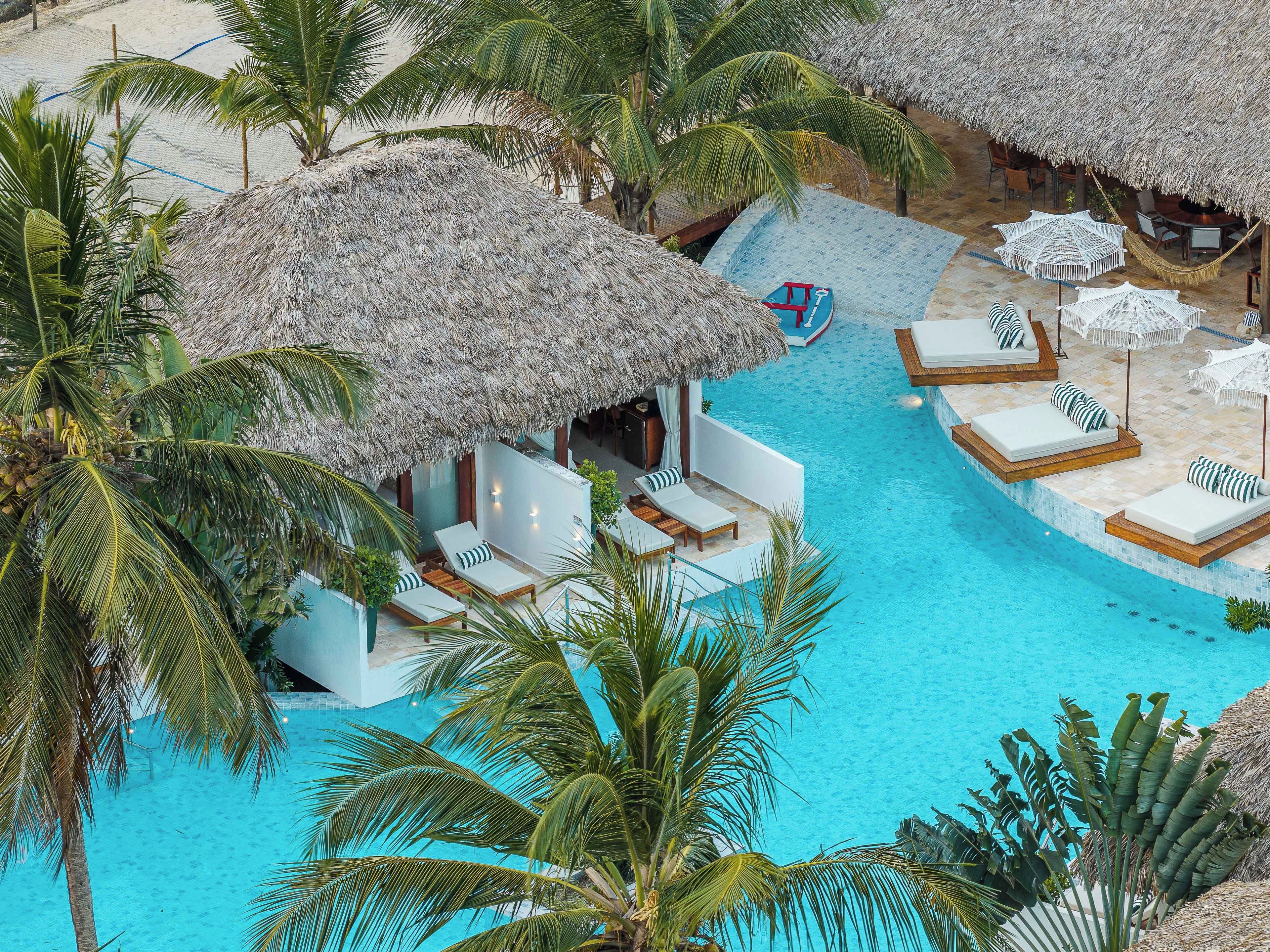 A resort with a swimming pool, thatched-roof structures, and lounge areas.