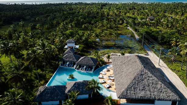 Ein Resort mit Pool, umgeben von strohgedeckten Gebäuden und Palmen.