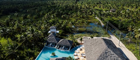 Ein Resort mit Pool, umgeben von strohgedeckten Gebäuden und Palmen.