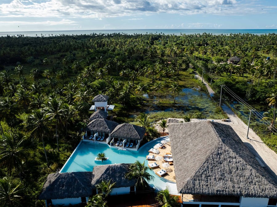 Resort com piscina cercada por construções de telhado de palha e palmeiras.