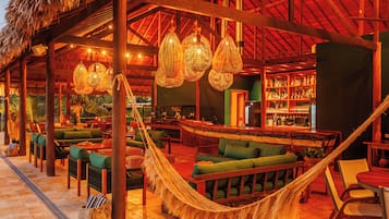 Zona de bar con temática tropical, que incluye mobiliario de mimbre, lámparas colgantes y una hamaca.