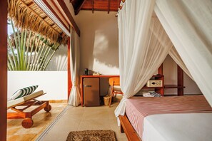 Un dormitorio con cama, escritorio, silla, refrigerador pequeño y ventana con vista a palmeras.