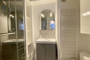 A modern bathroom with a glass shower enclosure, a white sink with a mirror above, and a white toilet.