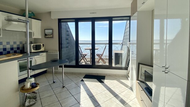 A modern kitchen with a view of the sea, a dining area with chairs, and a large sliding glass door.