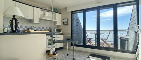 Une cuisine compacte avec vue sur la mer, un coin repas avec une table et des chaises, et une grande fenêtre.