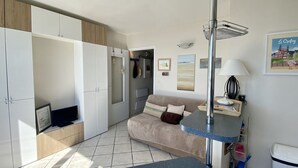 A modern hotel room with a sofa, TV, kitchenette, and artwork on the walls.