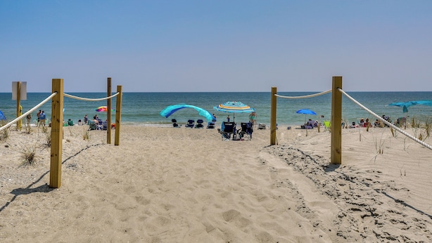 Una playa arenosa con postes y cuerdas de madera, sombrillas y gente.