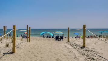 A sandy beach with wooden posts and ropes, umbrellas, and people.
