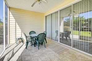 Une terrasse couverte avec une table et des chaises, un ventilateur de plafond et une porte-fenêtre coulissante donnant sur un espace extérieur.