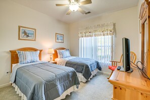 Une chambre avec deux lits, un ventilateur de plafond, une télévision et une fenêtre avec des rideaux.