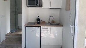 A compact kitchen with white cabinets, a built-in microwave, a small refrigerator, and a sink. - Gite "bambou" Avec Piscine (Beauvallon)