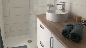 A modern bathroom with a glass shower enclosure, a wooden vanity with a sink, and a round mirror. - Gite "bambou" Avec Piscine (Beauvallon)